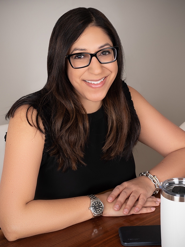 Portrait of Priya Bathija wearing glasses and seated at table.